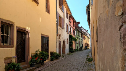 Obraz premium Narrow cobblestone street lined with centuries old stone houses in a charming Alsace village Riquewihr, quiet travel moments and authentic heritage atmosphere.