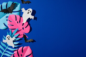 Naklejka premium Tropical Halloween paper ghosts bats and bright monstera leaves on blue background for party decor