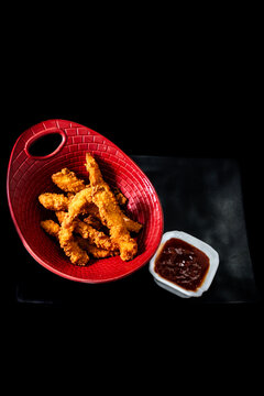 Fried chicken tenders in a textured red basket, ready for dipping in a side of sauce