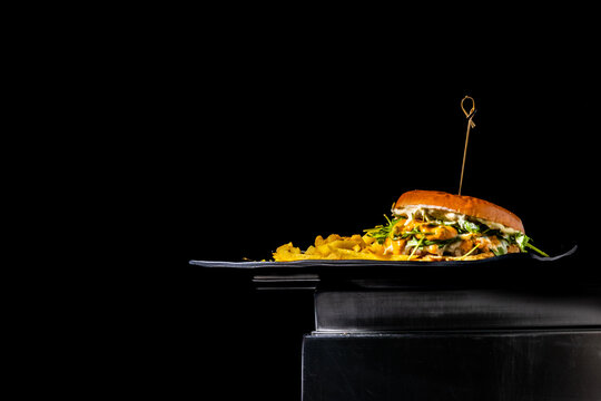 Loaded chicken burger with crispy french fries on a dark plate, studio shot
