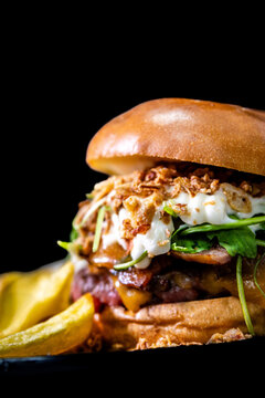 Gourmet burger with brioche bun, fried onions, cheese, bacon, arugula, and potato wedges