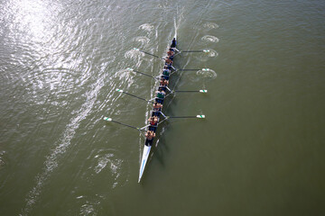 Top view of rowers paddling racing shell across reflective water during practice. © Shootdiem