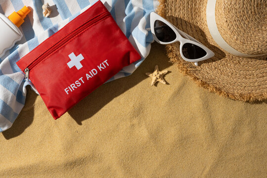 First aid kit and sun protection essentials on a sandy beach towel for safe summer travel