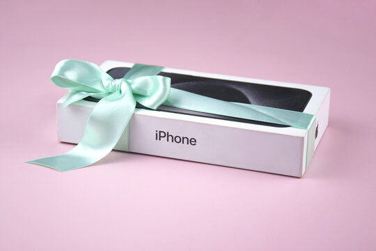 The box with an iPhone 15 Pro Max phone with a bow as a gift on a pink background.