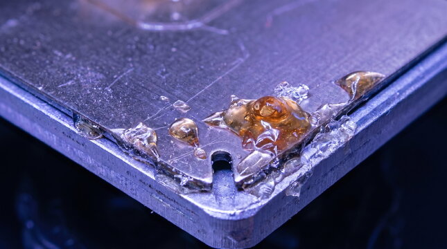 Macro close up of spilled amber liquid resin on the corner of a scratched metal 3d printer build plate under uv light