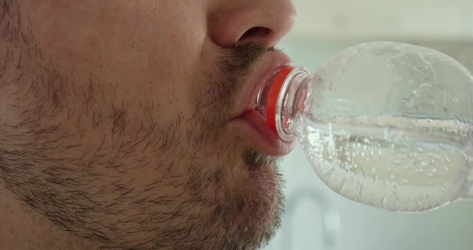 man drinking water directly from a plastic bottle with the entire bottle opening inside the mouth area. Suitable for hydration, thirst, drinking habits, refreshment, lifestyle, and beverage concepts.