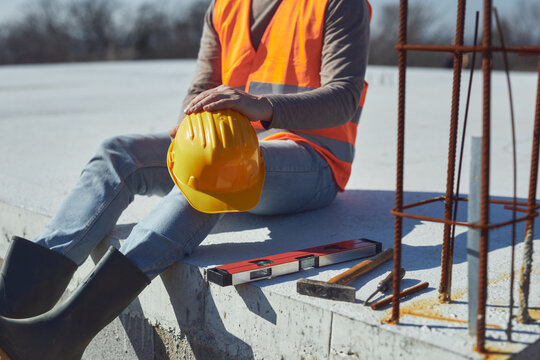 Construction worker working outdoors on a construction site, making a pause and holding a yellow hardhat.