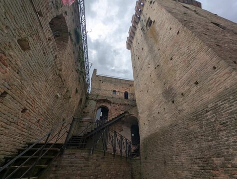 Torre medievale in mattoni ripresa dal basso, con merlature imponenti e atmosfera drammatica sotto un cielo grigio, ideale per contenuti storici e architettonici
