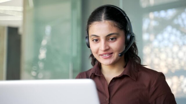 Young smiling woman corporate operator in headset working in customer support service on helpline telesale talking using laptop in business office. Agent of call center advises clients online Close up