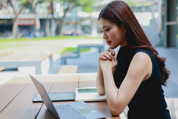 Fototapeta premium Southeast Asian office workers wearing black outfits and white coats collaborate in a green park setting. They use laptops and documents outdoors, blending professionalism productivity