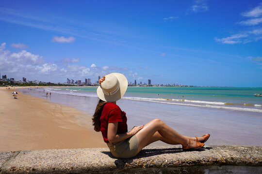 Rear view of woman sitting on wall enjoying Joao Pessoa beach on northeast coast of Brazil