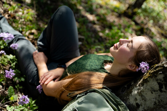 A young woman lies on the ground beneath a tree, enjoying peaceful silence and closed eyes in the forest. The concept of mindfulness and stress relief is embodied in nature.