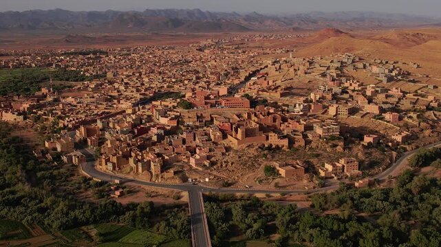 Tinghir in Draa-Tafilalet, Morocco, between the High Atlas and Jbel Saghro ranges, showing ksar districts, urban expansion, Phoenix dactylifera groves and arid valley terrain, orbit establishing shot.