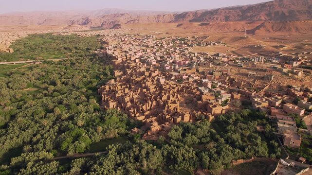 Tinghir in Draa-Tafilalet, southeastern Morocco, with mudbrick ksar districts, Phoenix dactylifera groves and Jbel Saghro mountain ridges near Todgha Valley, high panoramic establishing shot.