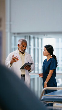 Veteran chief physician explaining digital patient charts to an attentive clinical nurse during corridor rounds.
