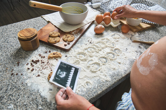 Expectant mother holding a sonogram while making cookies, symbolizing new life