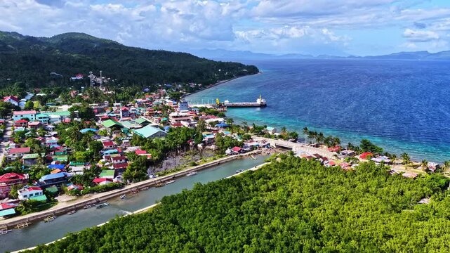 Beautiful wide drone shot over Padre Burgos in Southern Leyte, Philippines. Features a long river canal and thick mangrove forest running alongside a colorful coastal town and ocean harbor port.