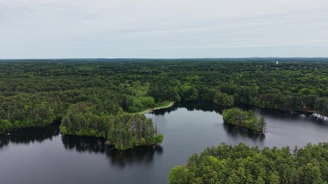 Lake and walking path surrounded by green forest Harold Parker State Forest, Massachusetts, Andover, United States. Aerial forward, copy space
