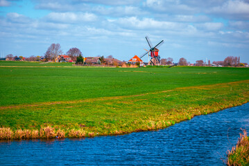 Fototapeta premium Vibrant green pasture and blue canal leading towards a traditional Dutch windmill in the countryside