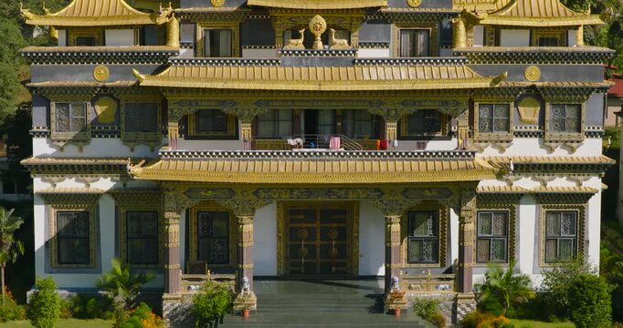 Drone down-to-top and push-in view of the golden roof of the Buddhist monastery building, in Pharping, Nepal, showing the green hillside in the background