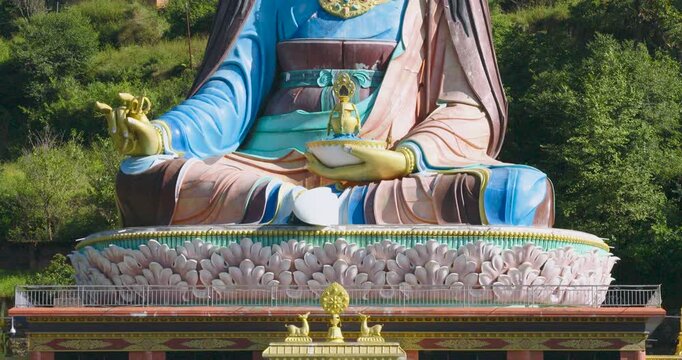 Drone moves from down to top, capturing a rising view of the large colorful Guru Rinpoche statue against the green hillside and mountain environment in Pharping, Nepal, Greenery views and bright sky