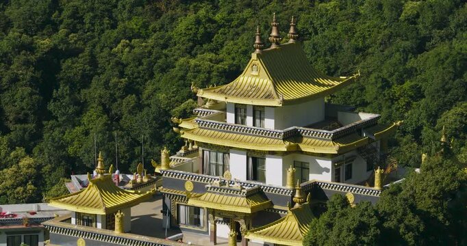 Drone slowly orbits the upper golden roof of the Buddhist monastery building in Pharping, Nepal, showing the green hillside background in the bright sunny day
