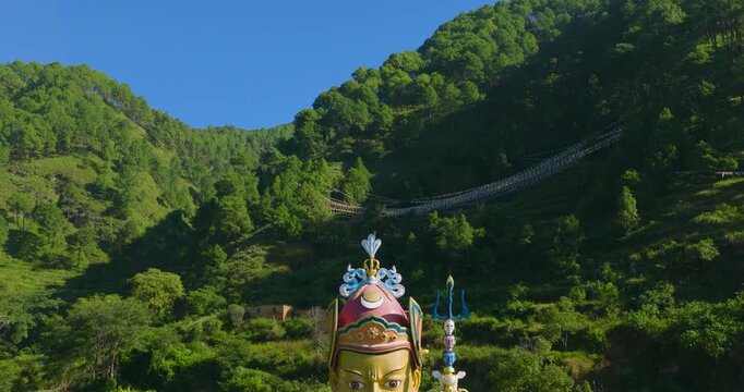 Drone pulls out backward from the large Guru Rinpoche statue located in Pharping, Nepal, revealing the green hillside landscape and surrounding valley scenery in the background.