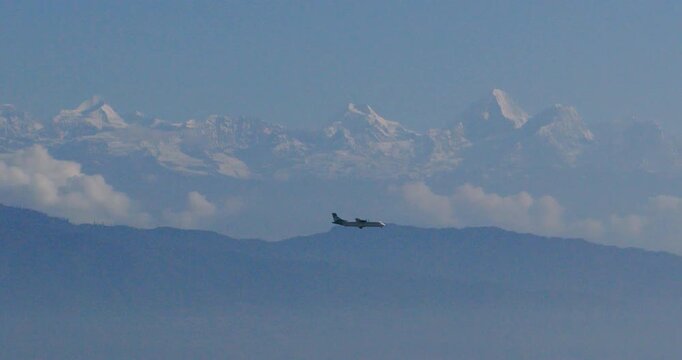 Drone moves sideways to track an airplane in flight, showing the aircraft moving across the sky with a snow-capped mountain range and clear blue sky in the background, seen from Pharping Nepal