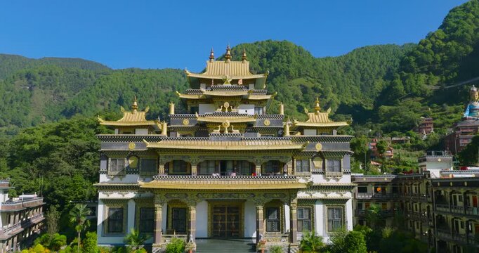Drone push-in view flying forward across the golden roofs of the Buddhist monastery building, in Pharping, Nepal with lush green hills rolling out in the background.