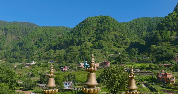 Drone pull-out view moving backward away from the lush green hills to reveal the majestic golden roofs of the Buddhist monastery building nestled in the scenic landscape of Pharping, Nepal.