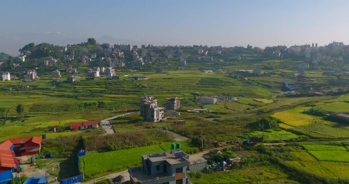 Drone moves forward and glides over a hillside landscape of green agricultural terraces and scattered rural village houses located in Pharping, Nepal