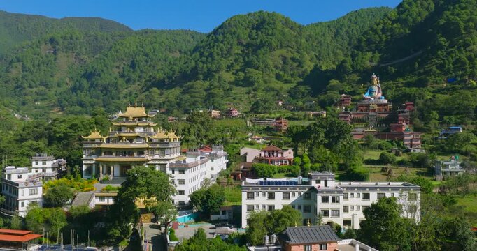Drone pushes forward over the valley scene, showing the golden Buddhist monastery building, the giant colorful Guru Rinpoche statue on the hill, Pharping, Nepal, surrounded by green hills