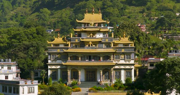 Drone pushes in toward the old golden Buddhist monastery building in Pharping, Nepal, showing the green hillside backdrop