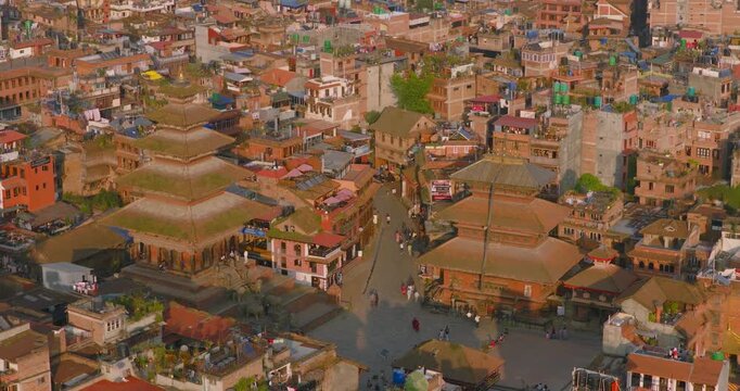 Drone tilts up to reveal Nyatapola and Bhairavnath temples alongside brick houses, a pedestrian plaza, and distant hills in Bhaktapur Darbar Square, Bhaktapur Nepal.