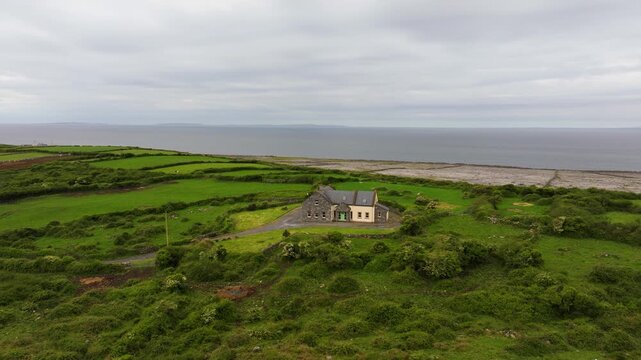 A solitary house stands surrounded by lush fields and a rugged coastline in The Burren. Perfect for real estate or travel promotions.