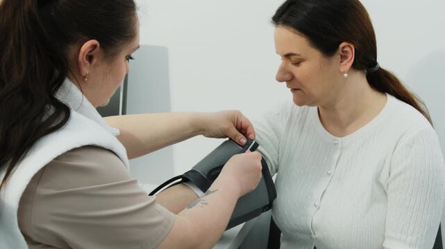 Nurse puts blood pressure monitor cuff onto woman arm in clinic. Female doctor examines patient cardiovascular health in hospital slow motion