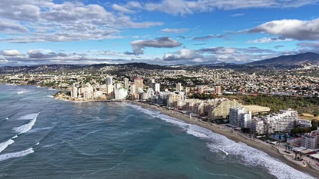 Aerial coastal cityscape, waves, beachfront skyline with highrise hotels and turquoise water drone glides