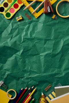 Vertical flat lay of back to school supplies. Top and bottom borders on a green crumpled paper