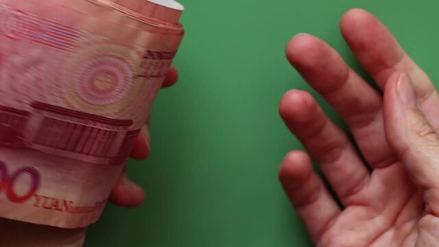 Close-up of hands holding Chinese one hundred yuan banknotes (CNY) or renminbi (RMB) above green surface. Saving money, financial income and growth, business concept.