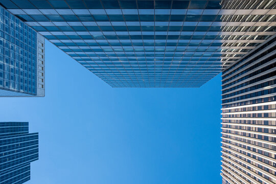 Looking upward in Paris, France, architecture frames tower, glass, sky, business facade and geometric office edges inside La Defense against blue space above