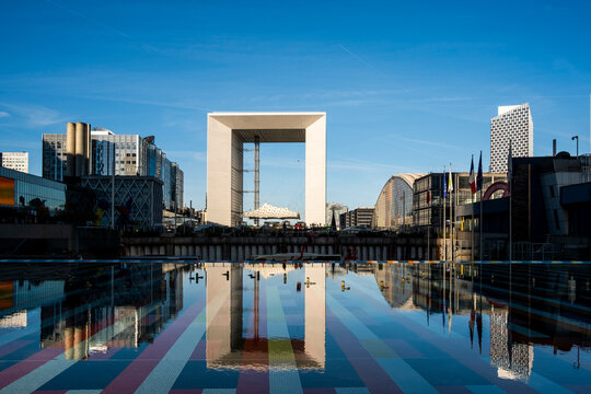 Grande Arche in Paris, France creates reflection across water as architecture, skyline, plaza, business and tower forms align within La Defense