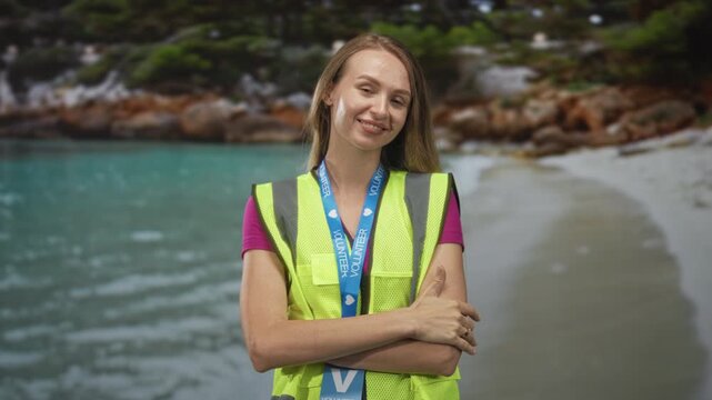 Woman wearing a fluorescent reflective vest raises two fingers in a peace sign and crosses her arms in front of a beach backdrop in a studio; community service pride.