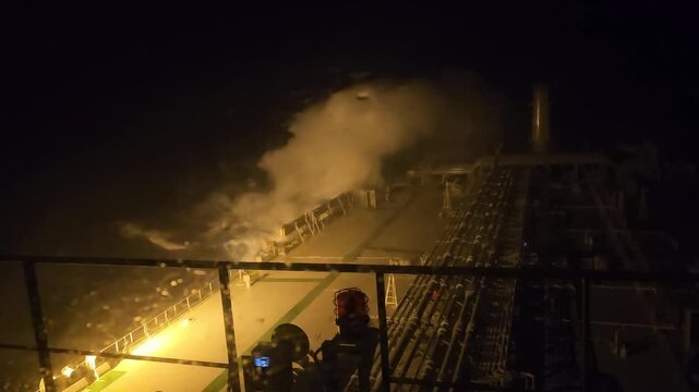 High angle nighttime view from a tanker ship bridge during a severe storm at sea, with powerful ocean waves breaking and crashing over the deck in pitch darkness. High quality FullHD footage
