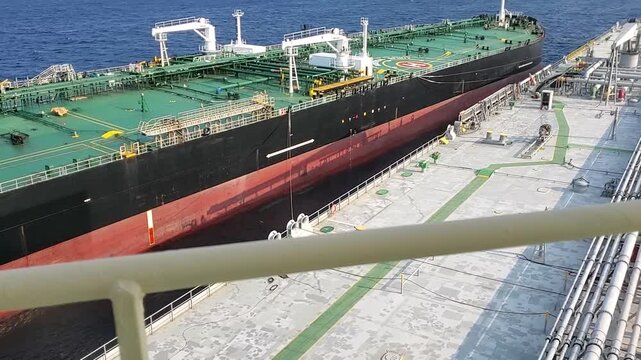 High angle view of a large industrial oil tanker ship during a ship to ship transfer operation, with mooring lines being tensioned between two vessels at open sea. High quality FullHD footage