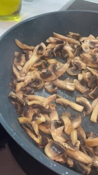 Vertical close up of sliced agaricus mushrooms browning in a hot nonstick frying pan with steam rising, showcasing the process of cooking a savory vegetarian meal. High quality 4k footage