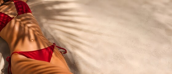 Fit woman in red bikini lying on sandy beach under palm leaf shadow with copy space