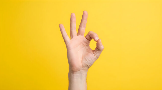 Hand making ok gesture on yellow background