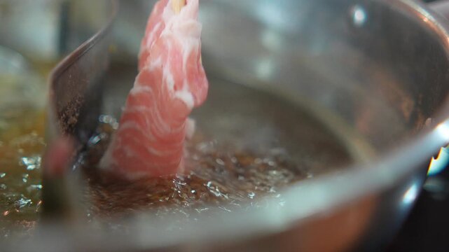 4K Close-up chopsticks dipping premium sliced pork into boiling broth in hot pot Shabu-shabu or sukiyaki dining experience, Asian food culture and delicious meal.