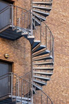 A spiral staircase wraps a brick facade, where metal stairs, exterior urban architecture and handrail carve a vertical escape route