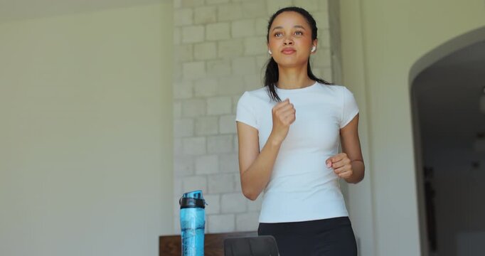 Athletic woman running on treadmill during home cardio workout in apartment interior. Burn calories concept.